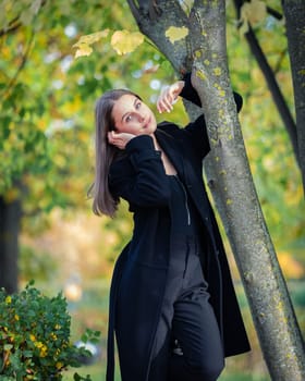 A beautiful girl stands by a tree in an autumn park