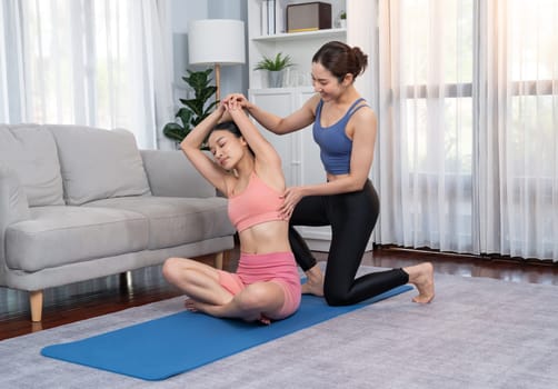 Asian woman in sportswear doing yoga exercise on fitness mat with trainer or workout buddy as home workout training routine. Healthy body care in yoga lifestyle people. Vigorous