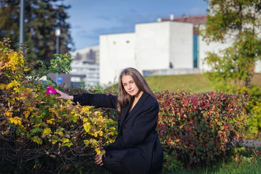 Portrait of a beautiful girl near a red-yellow bush in an autumn park