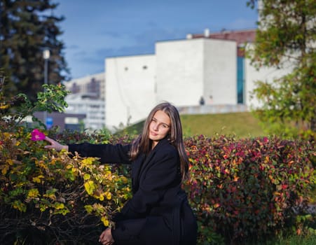 Portrait of a beautiful girl near a red-yellow bush in an autumn park