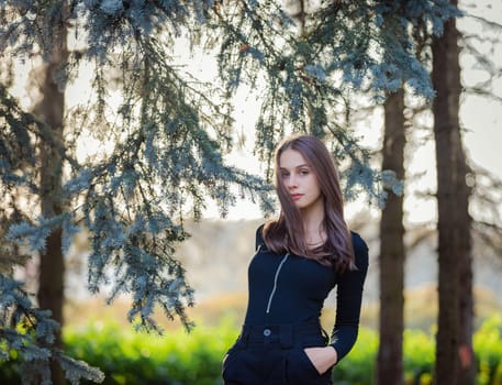 A girl stands near a blue spruce in an autumn park