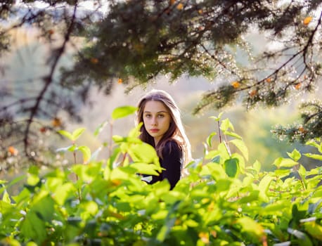 Beautiful girl in green foliage in the autumn park