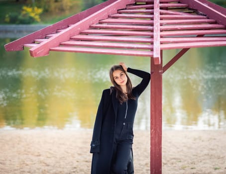 A beautiful girl poses while standing by a pond under an umbrella in an autumn park