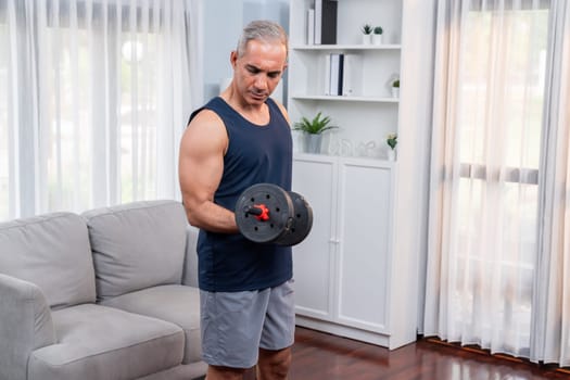 Athletic and sporty senior man engaging in body workout routine with lifting dumbbell at home as concept of healthy fit body with body weight lifestyle after retirement. Clout