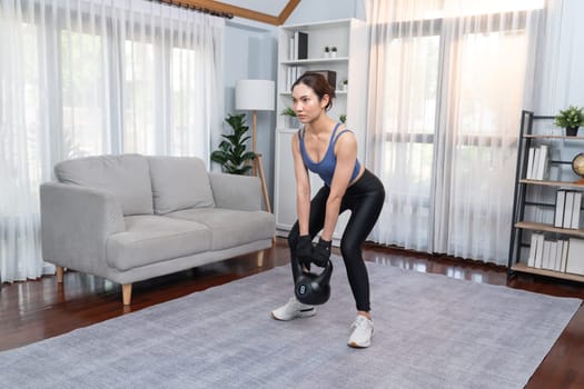 Vigorous energetic woman doing dumbbell weight lifting exercise at home. Young athletic asian woman strength and endurance training session as home workout routine.