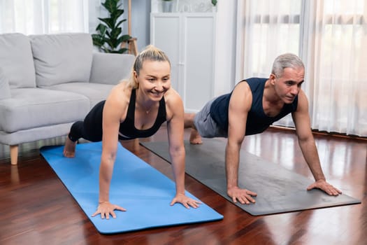 Athletic and active senior couple doing exercise on fit mat with plank climbing together at home exercise as concept of healthy fit body lifestyle after retirement. Clout