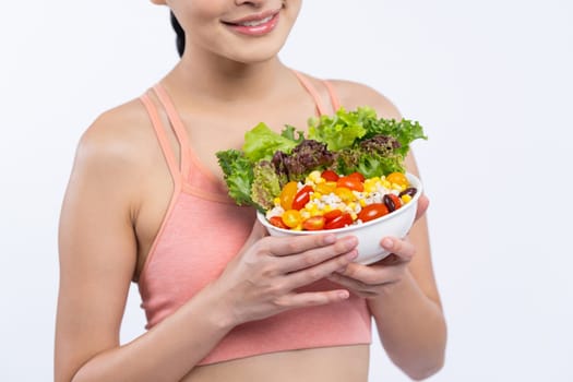 Young sporty Asian woman in sportswear holding salad bowl fill with vibrant of fruit and vegetable. Natural youthful and fit body lifestyle with balance nutrition on isolated background. Vigorous