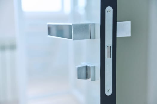 Close-up of a chrome modern door handle on a white glossy door. Modern minimalism style, door furniture, interior details