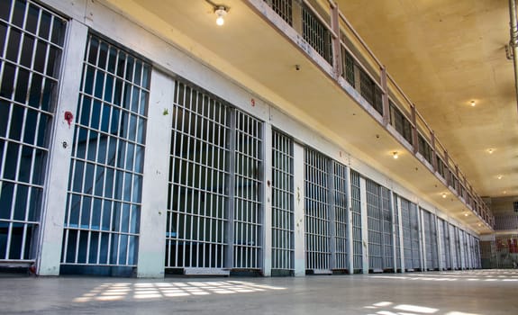 A prison cell block with many cells and bars. The bars are very tall and the windows are small