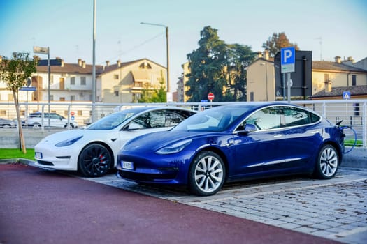 Cremona, Itally - October 6th 2024 Two tesla model 3 electric cars, one in blue and one in white, parked in a designated charging area