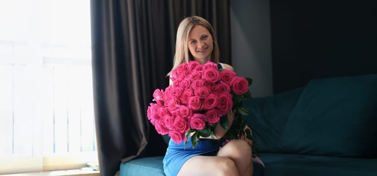 A young woman is sitting on a sofa with a large bouquet of roses, close-up. Romance, holiday greetings, wedding anniversary