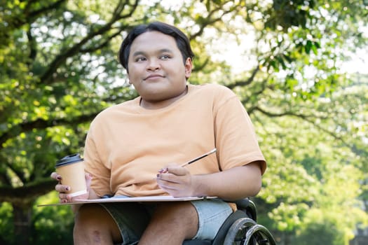 A young artist in a wheelchair holds a coffee cup and sketchpad, enjoying a creative session in a vibrant, green park.
