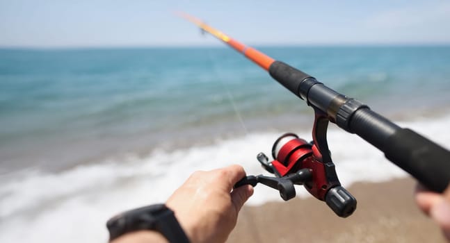 Hands hold a fishing rod against the background of the sea coast, close-up, blurry. Fishing from the shore, spinning, sports