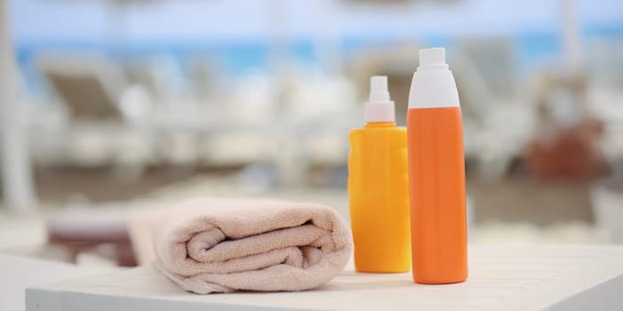 Orange plastic bottles and a beige towel on a beach lounger, close-up, blurry. Cosmetics for sunbathing and relaxation at sea