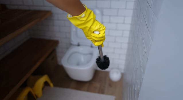 A hand in a rubber glove with a toilet brush in the toilet, close-up, blurred. Disinfection of plumbing fixtures, removal of dirt and plaque