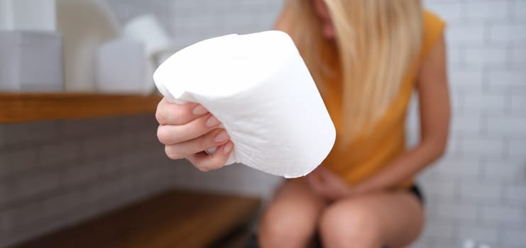 A woman is sitting on the toilet with toilet paper in her hand, close-up, blurry. Abdominal pain, diarrhea, constipation