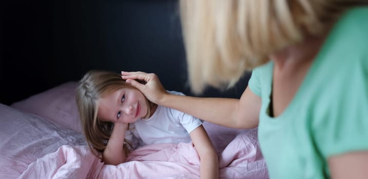 Mom strokes the child on the head, close-up. The daughter sits on the bed, the woman calms the girl
