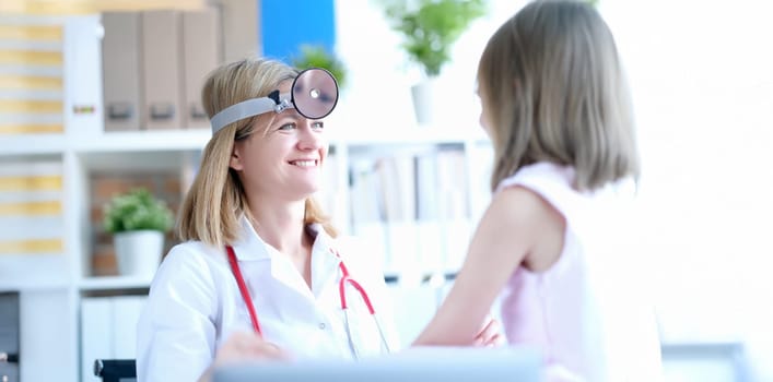 Female doctor at the clinic smiling at the little girl. Children's otolaryngologist, diagnostics of throat diseases