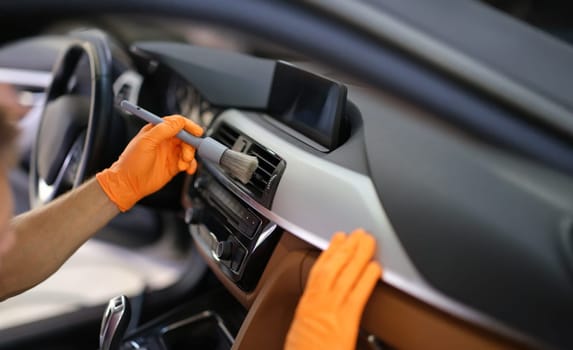 Hands in gloves with a dust brush, close-up. Cleaning between the vents in the machine. Car interior cleaning