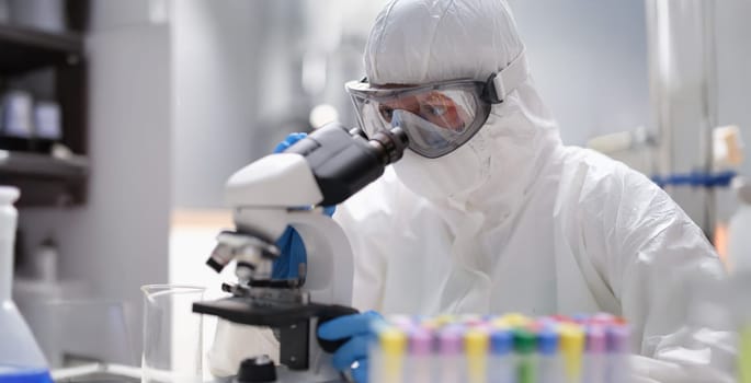A man in a protective uniform looks through an X-ray microscope, close-up. Laboratory equipment, quality assessment