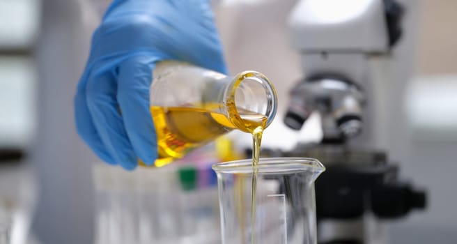 A hand in a glove pours a yellow liquid in the laboratory, close-up, blurry. Optical microscope, urine analysis