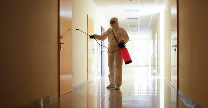 A man in uniform sprays a wall of a building from a balloon, close-up. Treatment of the corridor with an antibacterial agent