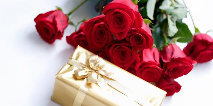 Gift wrapped in gold and a bouquet of red roses, close-up. Beautiful fighting box with ribbon, floristry