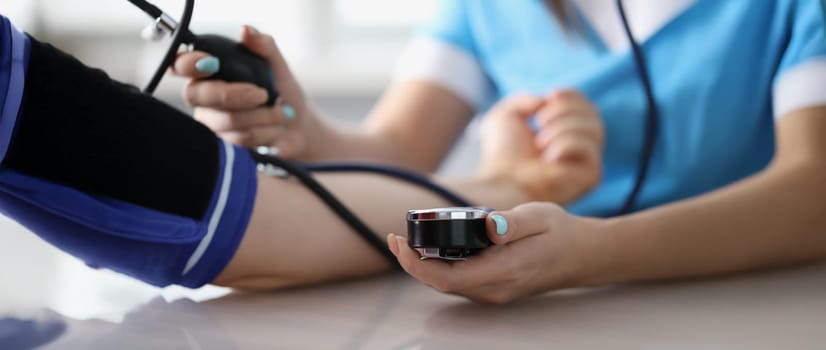 Close-up of doctor measuring patients blood pressure with tonometer tool on planned appointment. Health checkup at family doctor. Medicine, help concept