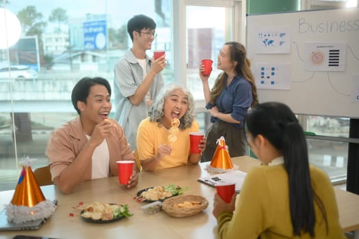 Cheerful corporate colleagues enjoying snacks and drinks during a lively office party.