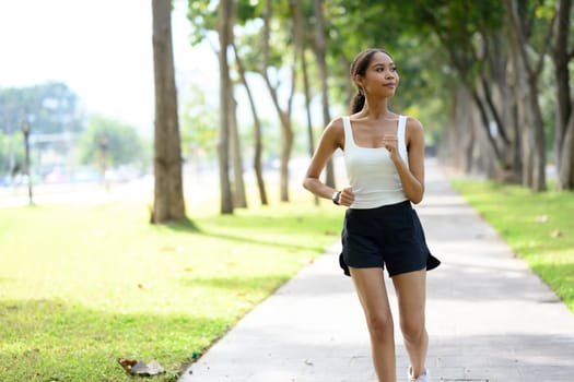 African American sportswoman jogging along shaded park pathway on a sunny day.