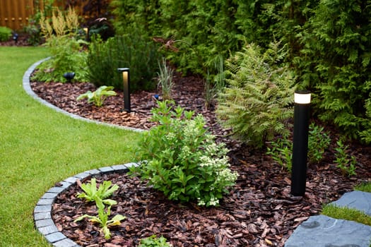 A beautifully serene garden featuring vibrant greenery, elegant twinkling lights, and decorative mulch pathways