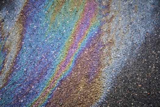 Gasoline or oil spill on asphalt creating rainbow pattern. Colorful gasoline or oil spill creating a rainbow pattern on asphalt, indicating pollution and environmental damage.