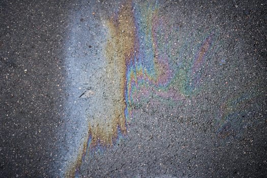 Gasoline rainbow creating colorful pollution on asphalt road.