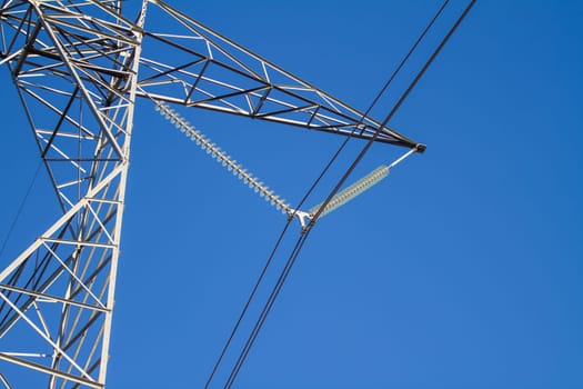 A tall power line tower with a blue sky in the background. The sky is clear and bright, and the tower is the main focus of the image