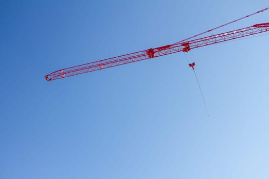 A crane is suspended in the air, with a red cable attached to it. The sky is clear and blue, with no clouds in sight. The crane is a large, red structure, and it is suspended high in the air