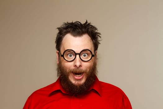 A man with glasses and a beard is smiling and looking surprised. He is wearing a red shirt