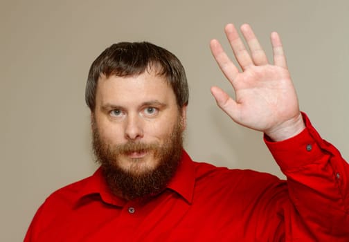 A man with a beard and red shirt waves his hand. The man's facial expression is serious and he is in a contemplative mood