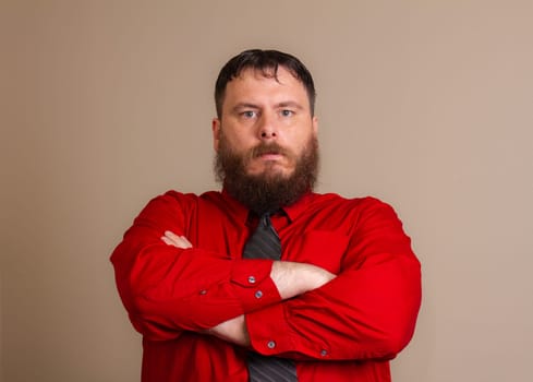A man with a beard and a red shirt is standing with his arms crossed. He is wearing a black tie