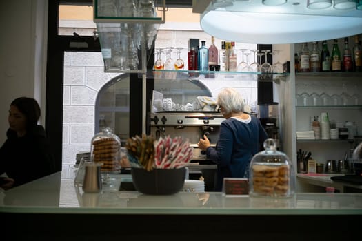 Cremona, Italy - November 20th 2024 Barista using coffee machine in a cafe in cremona, italy, with pastries and glasses on display