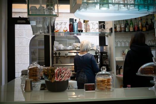 Cremona, Italy - November 20th 2024 Two baristas working behind the counter of a traditional italian bar, preparing coffee and snacks for customers