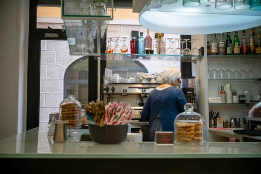 Cremona, Italy - November 20th 2024 Senior barista making coffee in a typical italian cafe in cremona, with biscuits and pastries displayed on the counter