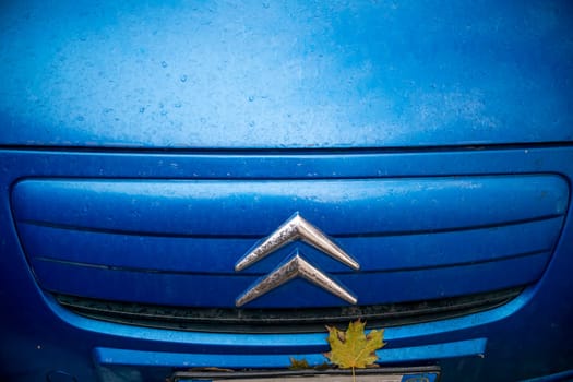 Lombardy, Italy - November 20th 2024 Close-up of the logo of a blue citroen c3 pluriel with a dry leaf stuck on the grille on a rainy autumn day
