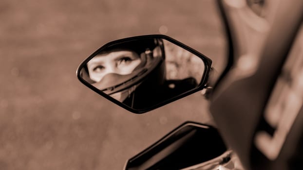 The girl on motorcycle. Blurred reflection in mirror. Selective focus. Colour of the year Mocha Mousse. Displaying girls in the mirror of the motorcycle