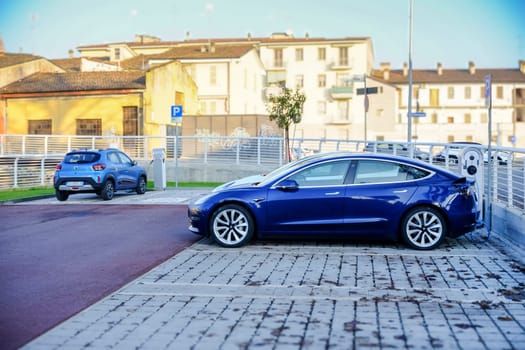 Cremona, Itally - October 6th 2024 Deep blue metallic tesla model 3 long range, 2021, charging batteries in a public charging station, with a renault zoe behind