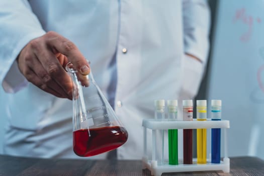 Close-up of a scientist handling a beaker with red liquid in a laboratory. Includes safety goggles and test tubes, emphasizing research, chemistry, and laboratory safety