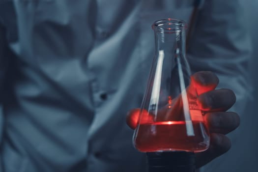 Close-up of a scientist holding a flask containing glowing red liquid, highlighting the intensity of the experiment and the scientific research process