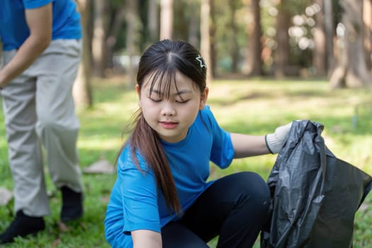 Young Asian girl in a park picking up litter during a community volunteer event focused on environmental awareness.