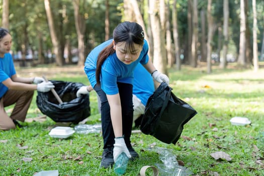 Asian girl volunteering in a park, picking up plastic waste during a family led environmental cleanup focused on sustainability.