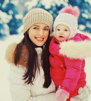 Winter portrait happy smiling mother and baby on hands over snowy christmas tree background
