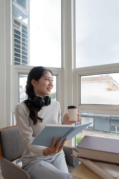 Young beautiful woman asian holding coffee and read a book while relax during work at home.